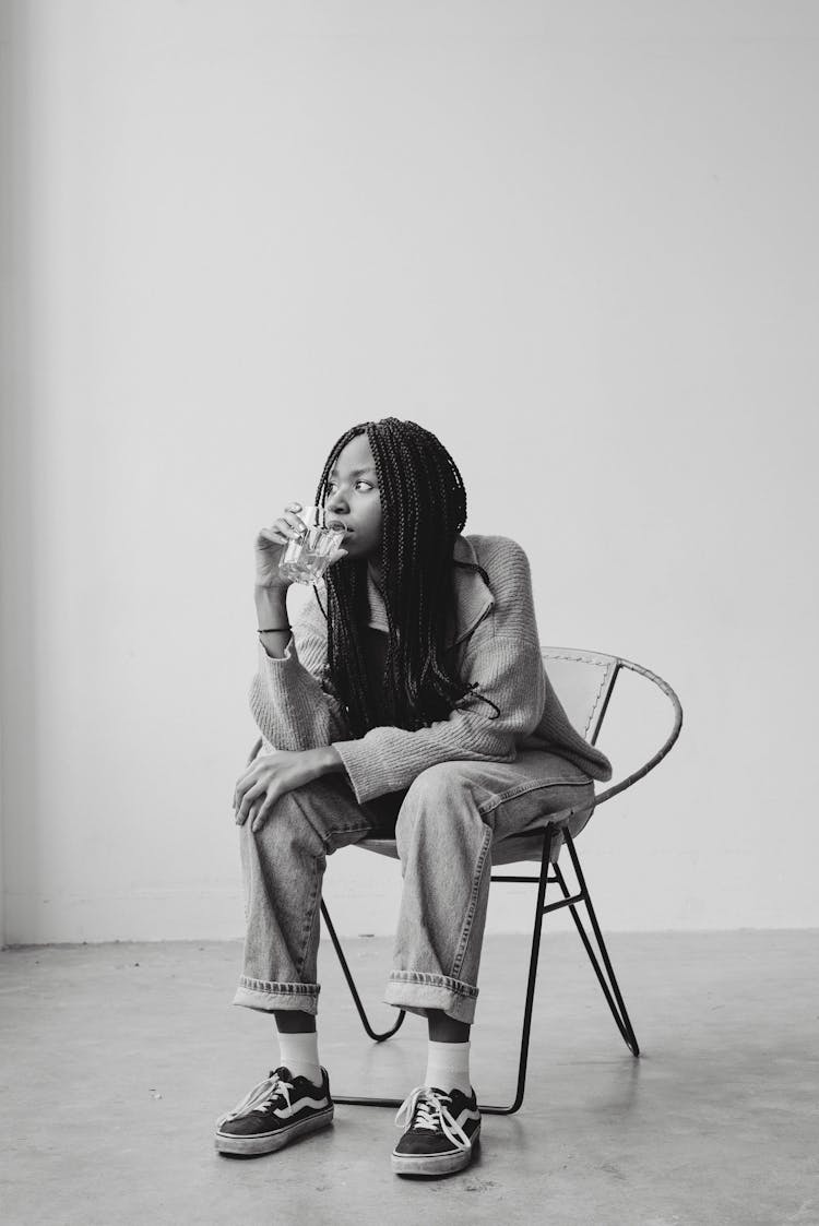 Pensive Black Female Sitting On Chair And Drinking Glass Of Water