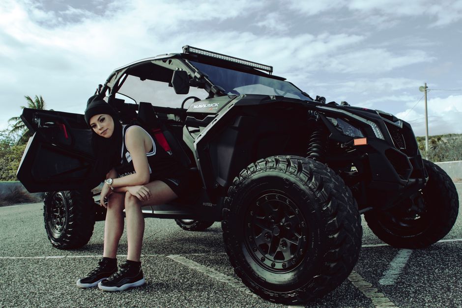 A stylish woman posing with a rugged off-road vehicle in an urban environment, showcasing adventure and fashion.