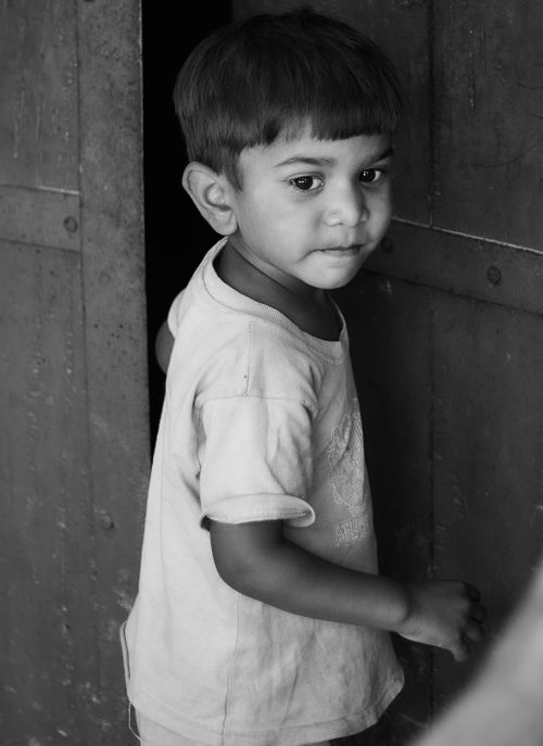 Free A candid black and white portrait of a young boy standing near a door, showcasing innocence and curiosity. Stock Photo