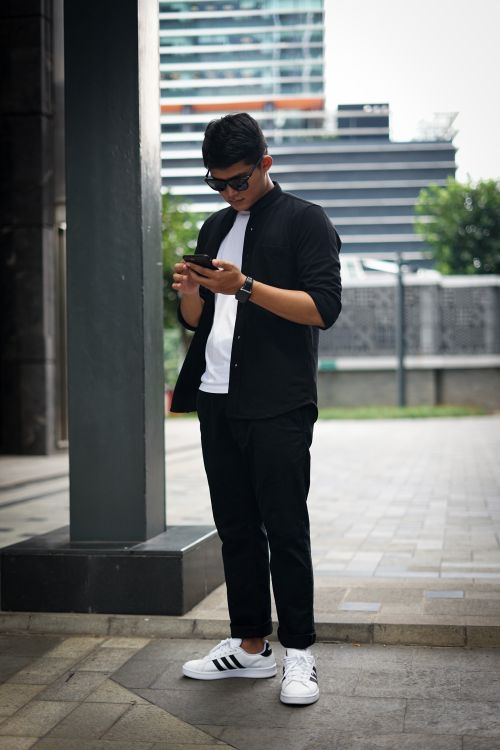 Free Stylish young adult standing by modern buildings using a smartphone. Stock Photo