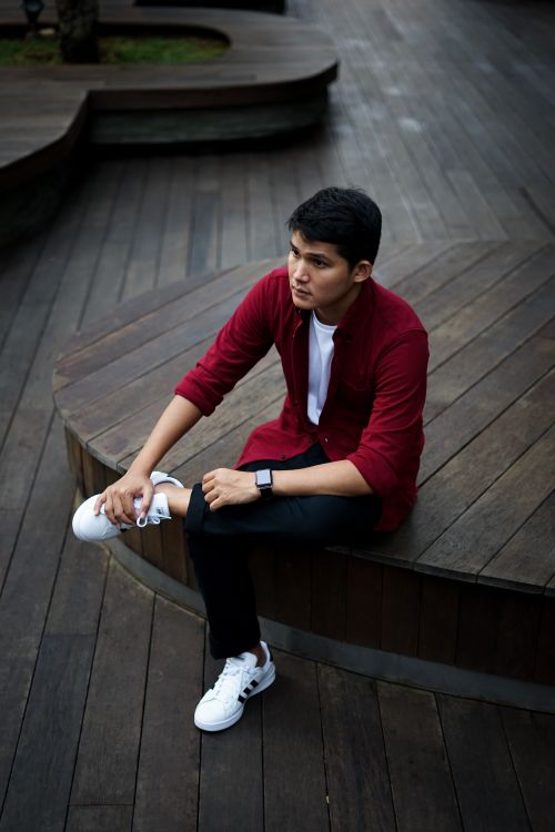 Free Fashionable man in red shirt sitting on a wooden deck, showcasing a trendy look. Stock Photo