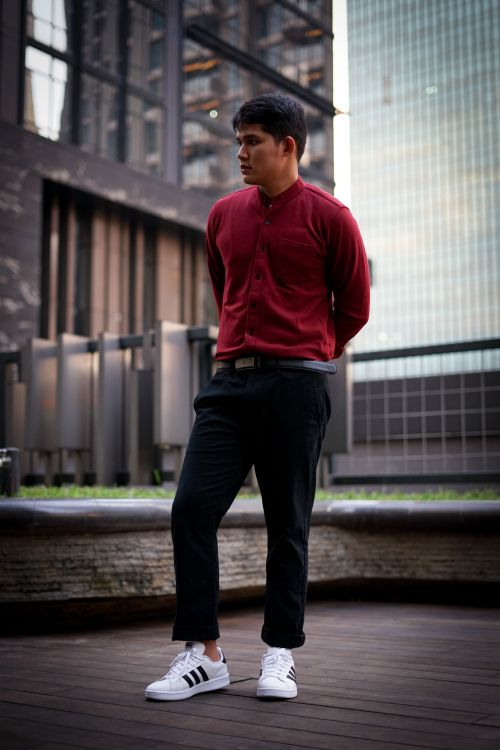 Free Fashionable man posing in a modern urban setting wearing a red shirt and sneakers. Stock Photo