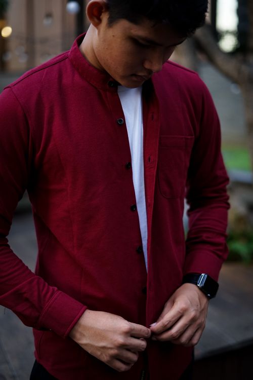 Free A man wearing a red shirt and smartwatch buttons his shirt outdoors. Stock Photo