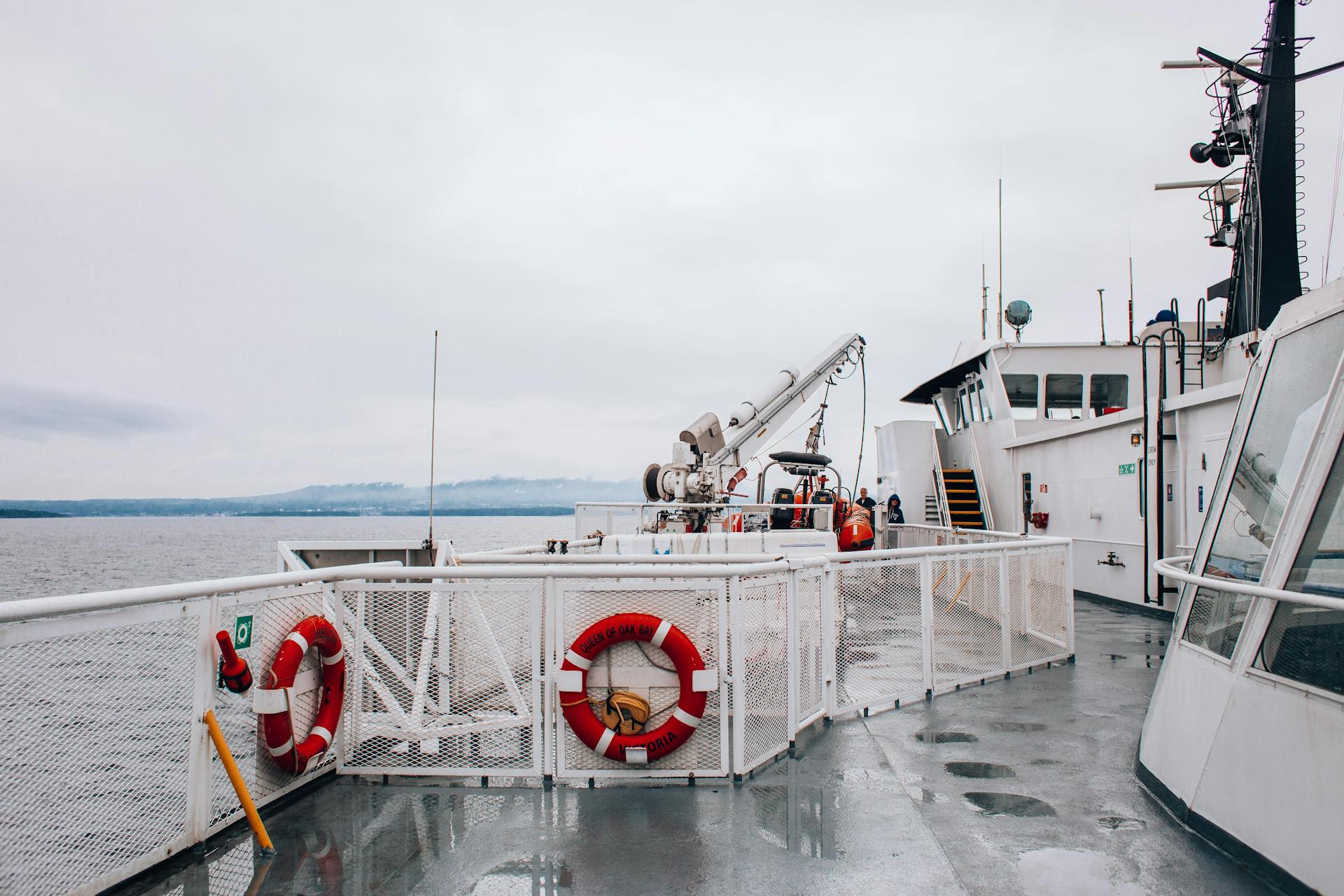 View of the ferry deck with lifebuoys and a calm ocean, under a gray sky.