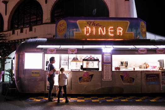 Evening scene with a father and daughter ordering at a neon-lit retro diner food truck.