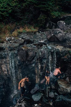 Three adventurers enjoy a refreshing dip at a secluded rocky waterfall.
