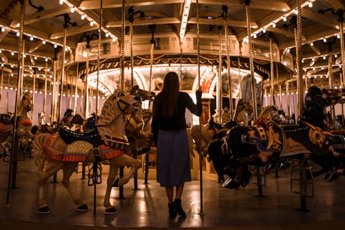 Free A woman stands by an illuminated carousel horse at night, creating a magical ambiance. Stock Photo