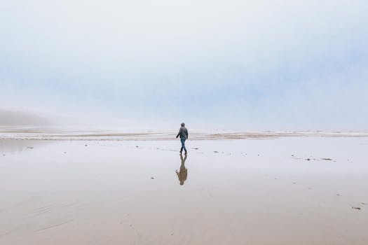 A solitary figure walking along a misty beach shore, creating a calm and serene atmosphere.