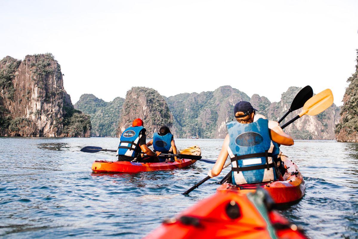 Travelers wearing life jackets paddle kayaks between limestone islands in Ha Long Bay