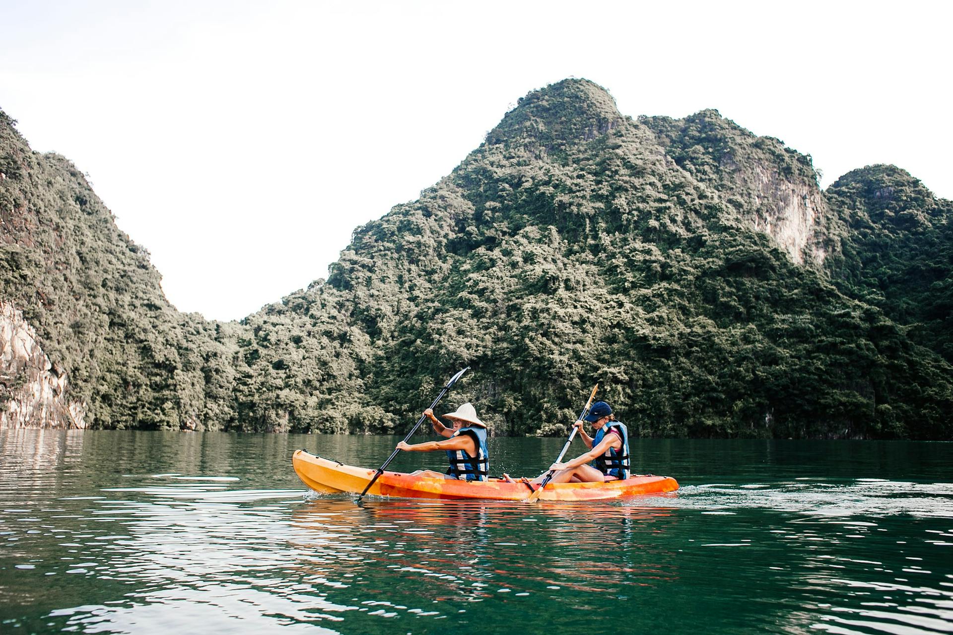 Two people kayaking on a tranquil lake surrounded by stunning mountain scenery, perfect for summer outdoor sport activities.