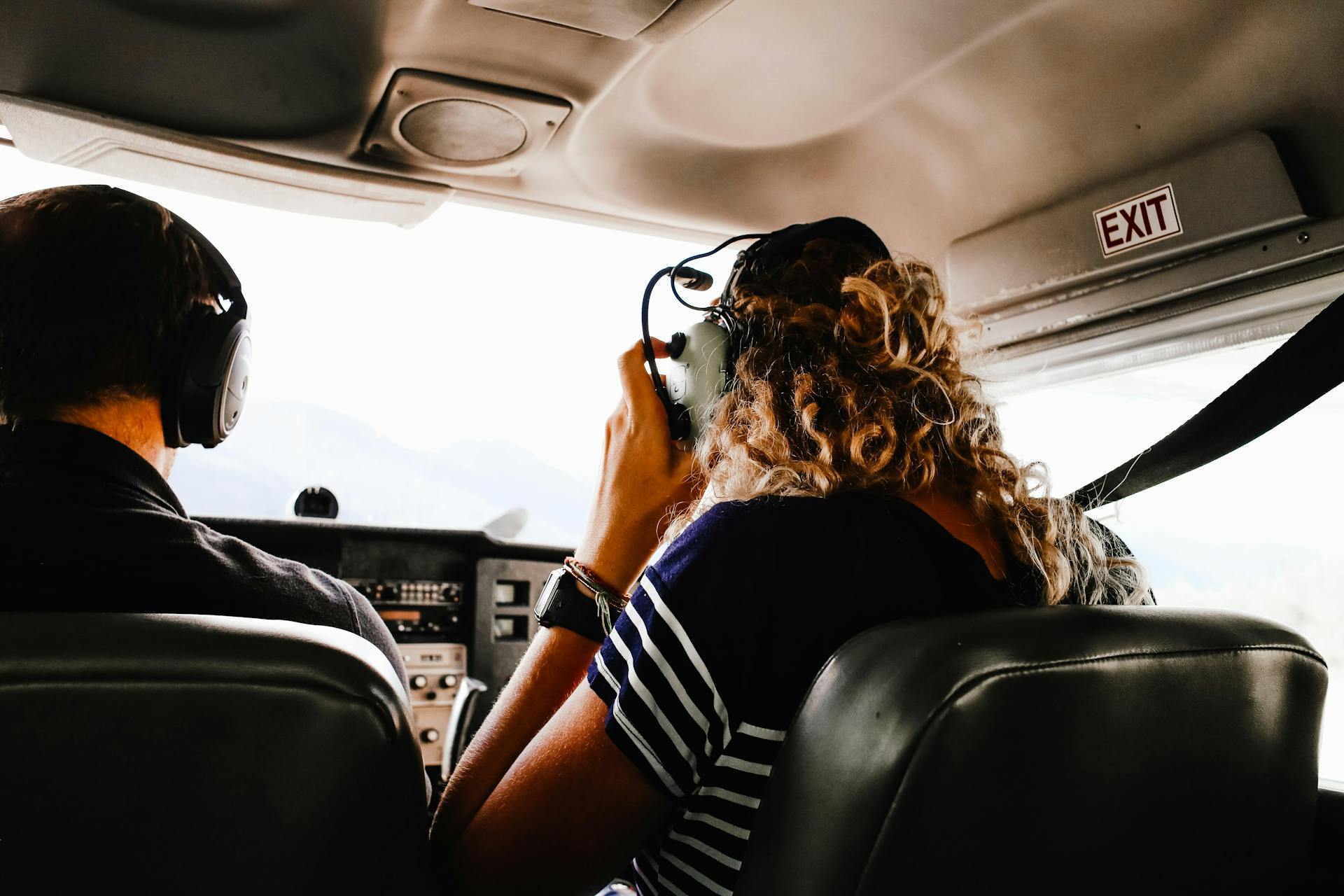 Two pilots in cockpit wearing headsets, viewed from behind. Engaged in flight operations.