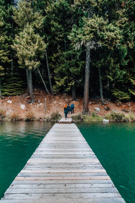 Couple walking on dock by tranquil forest lake, serene and picturesque.