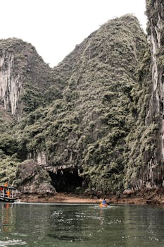 Kayaker exploring a dramatic limestone cave entrance in Halong Bay, Vietnam.