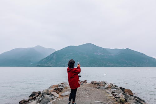 A Woman in Red Jacket Taking Photos Using a Smartphone