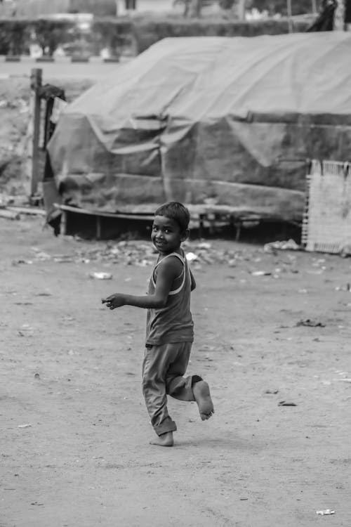 Grayscale Photo of a Happy Boy Running Barefoot