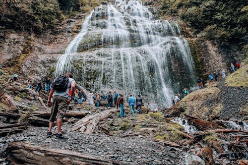 People Standing on a Brown Rock near the Waterfall