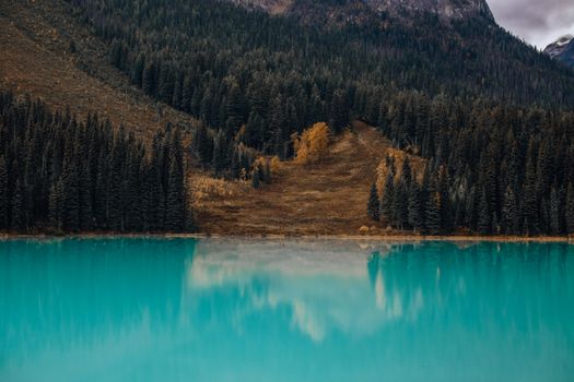 A serene turquoise lake reflecting a dense forest and mountain ridge.