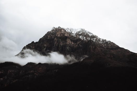 Dramatic view of a moody, foggy mountain with snowcapped peaks.