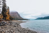 令人惊叹的岩石湖岸景色，背景是秋天的树木和雾蒙蒙的山脉