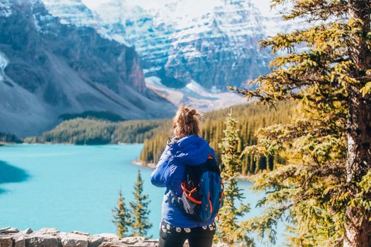 A woman in warm clothing overlooks a stunning mountain lake landscape in fall.