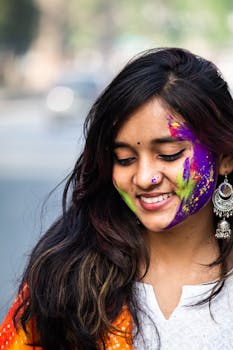 Smiling Indian woman with colorful gulal powder on face celebrating Holi outdoors.