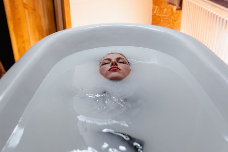 Person Lying In Bathtub With White Water