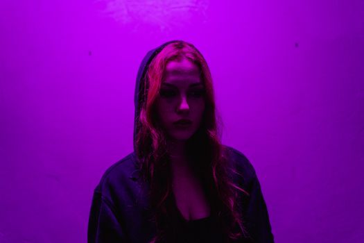 A woman in a hoodie stands under dramatic purple lighting, evoking emotion.