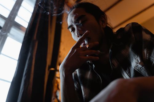 Free A man deep in thought while smoking a cigarette indoors, low lighting. Stock Photo