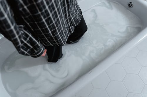 Person in Black Long Sleeve and Pants Standing on a White Bathtub