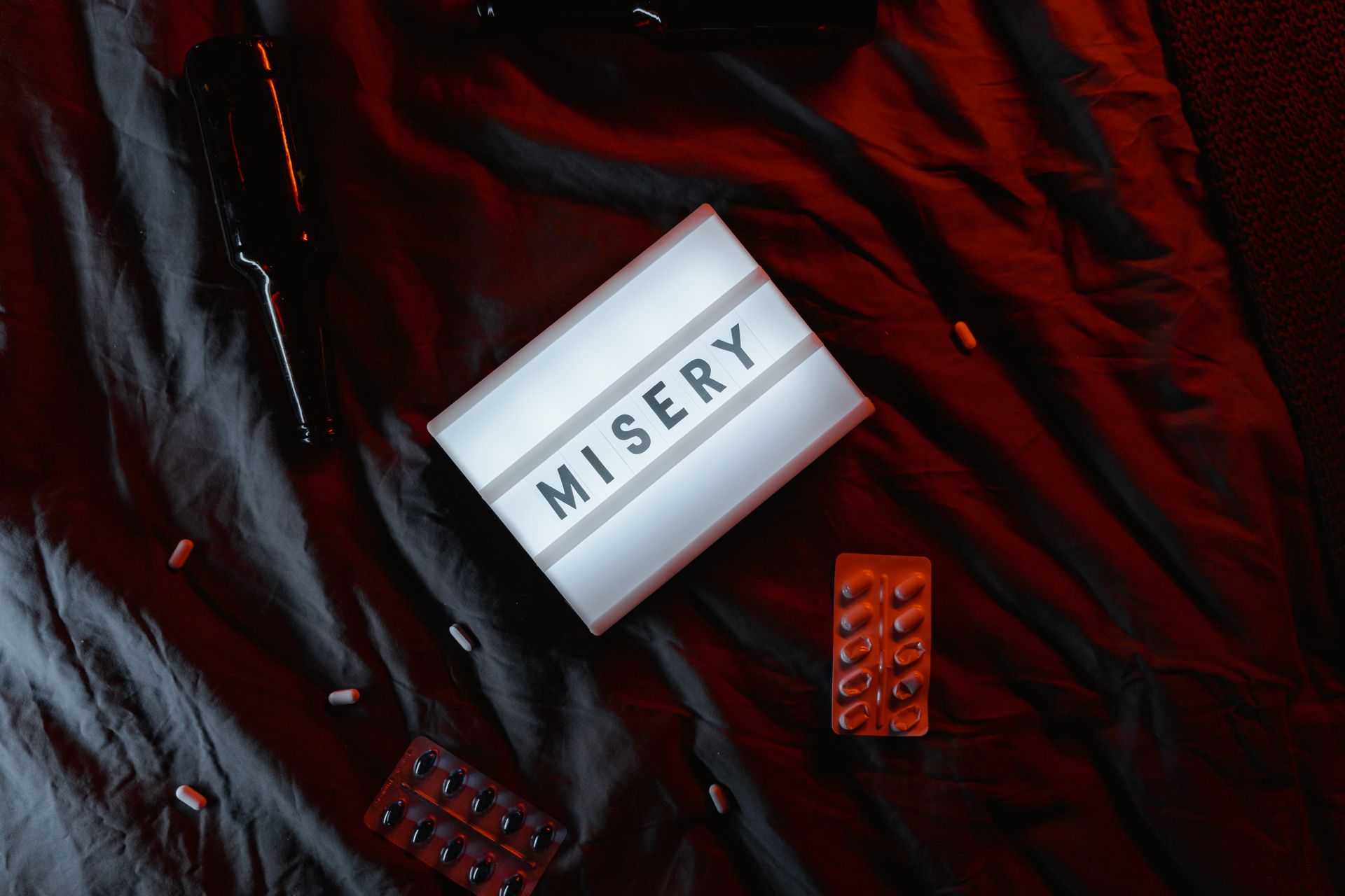Dramatic scene highlighting misery with a lightbox sign and scattered pills on a dark surface.