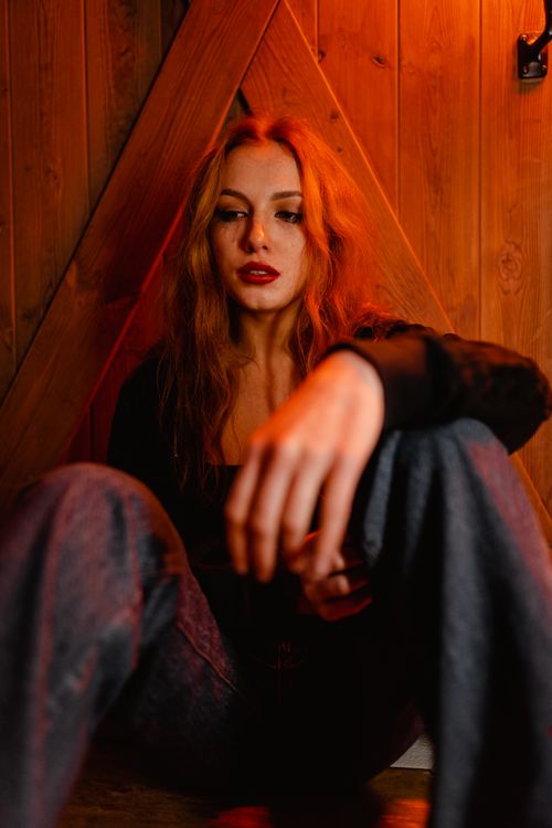 Free A young woman with a thoughtful expression sitting indoors, captured in warm lighting. Stock Photo