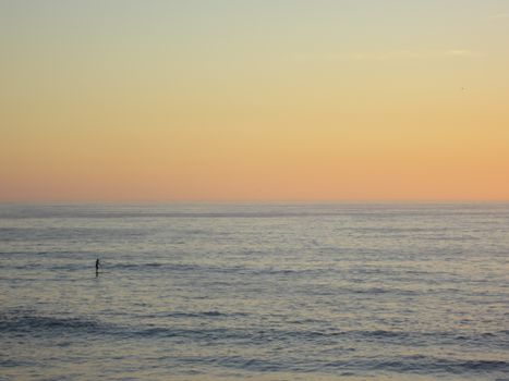 Tranquil ocean scene at sunrise with a lone paddleboarder on calm waters.