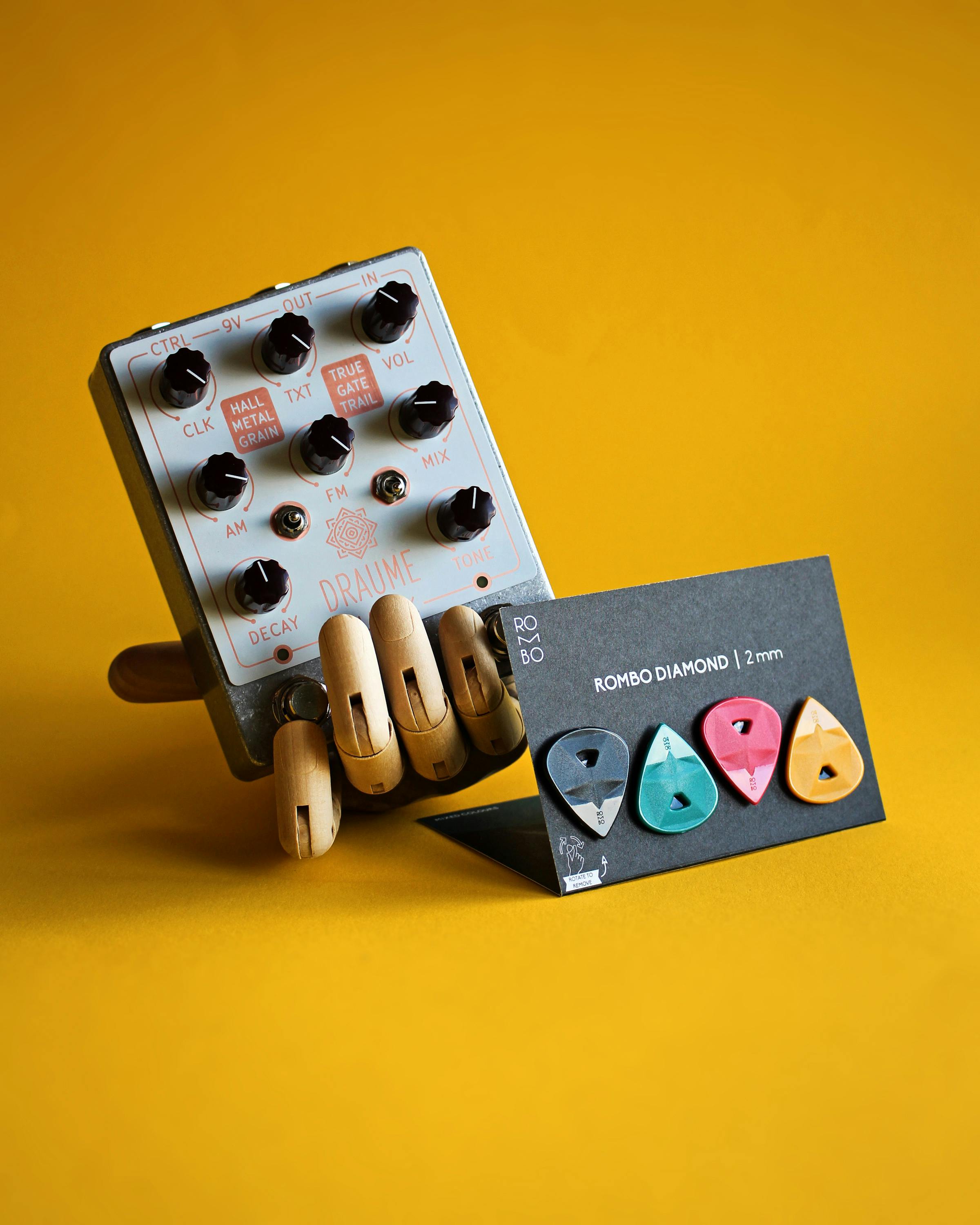Close-up of a guitar effects pedal with colorful picks on a vibrant yellow background.