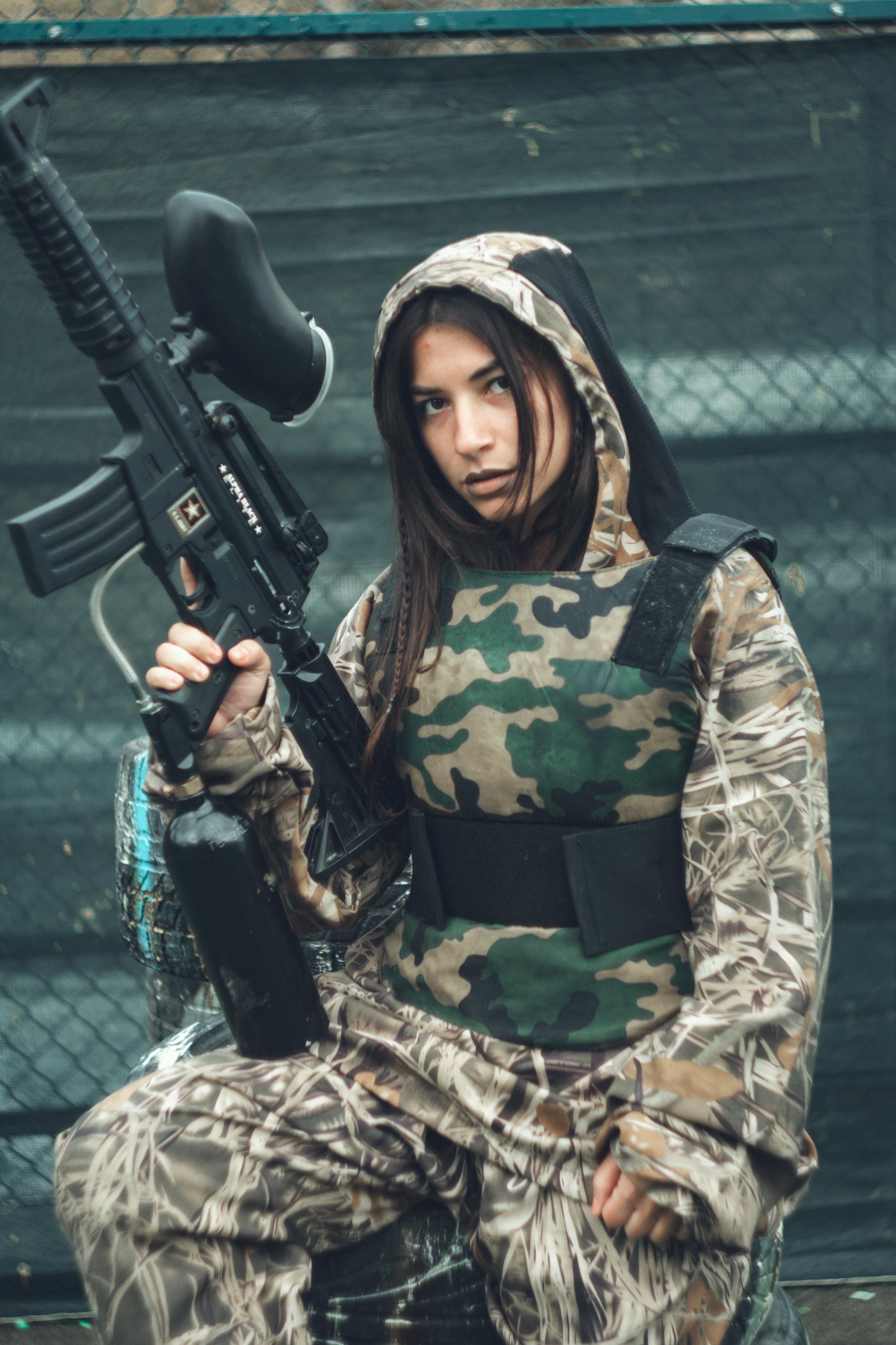 A young woman in camouflage gear holding a paintball gun, ready for action outdoors. Prescription Goggle Inserts - A young woman in camouflage gear holding a paintball gun, ready for action outdoors.