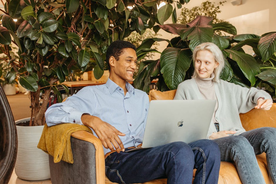 SoFi vs Marcus: Emergency Fund Strategy Explained Two colleagues sharing ideas and smiles while working on a laptop in a lively office setting.
