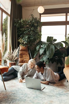 Two colleagues working together in a cozy, greenery-filled office space, focused and smiling.