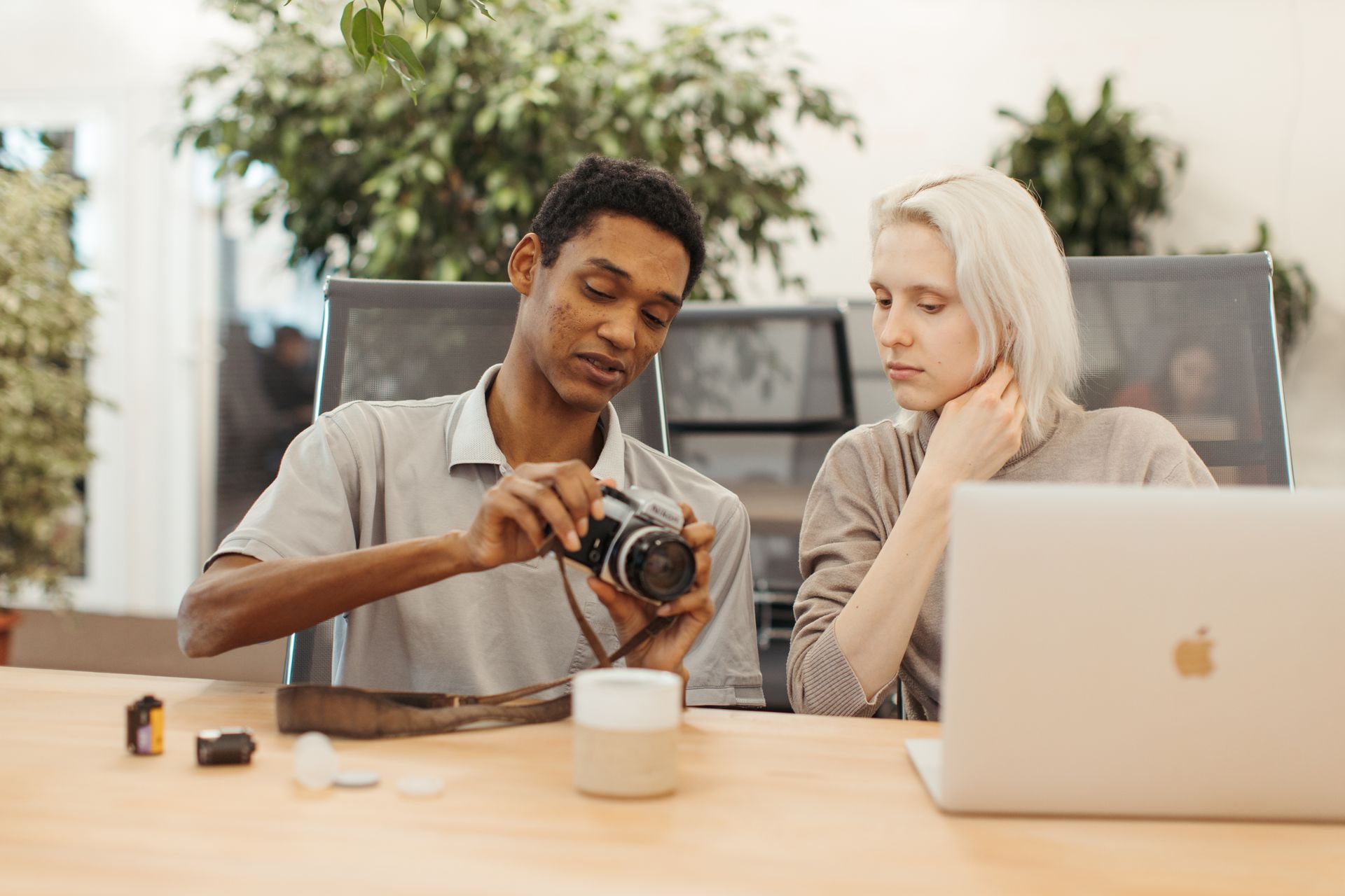 Two young adults discussing camera settings over a laptop in a modern office setting.