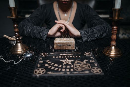 Person engaging in a mystical seance with a Ouija board and candles, creating an eerie atmosphere.