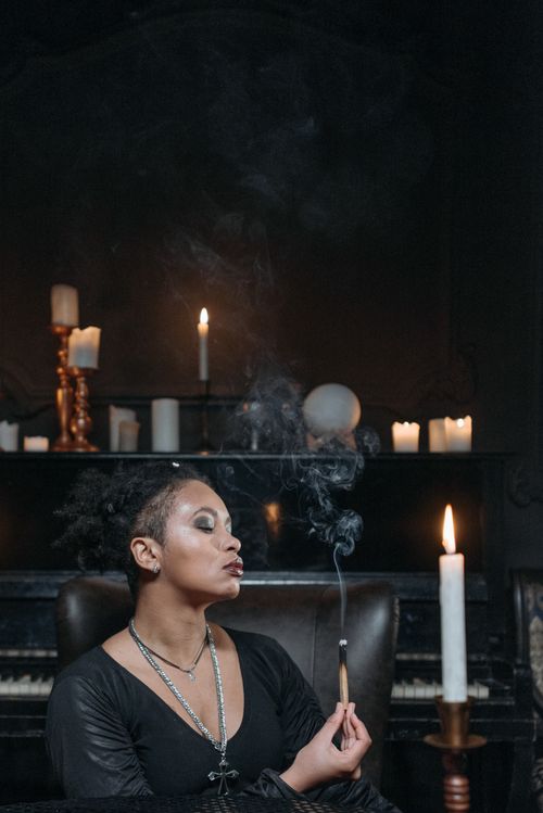 Free Portrait of a woman with smoke incense, surrounded by candles in a dimly lit room. Stock Photo