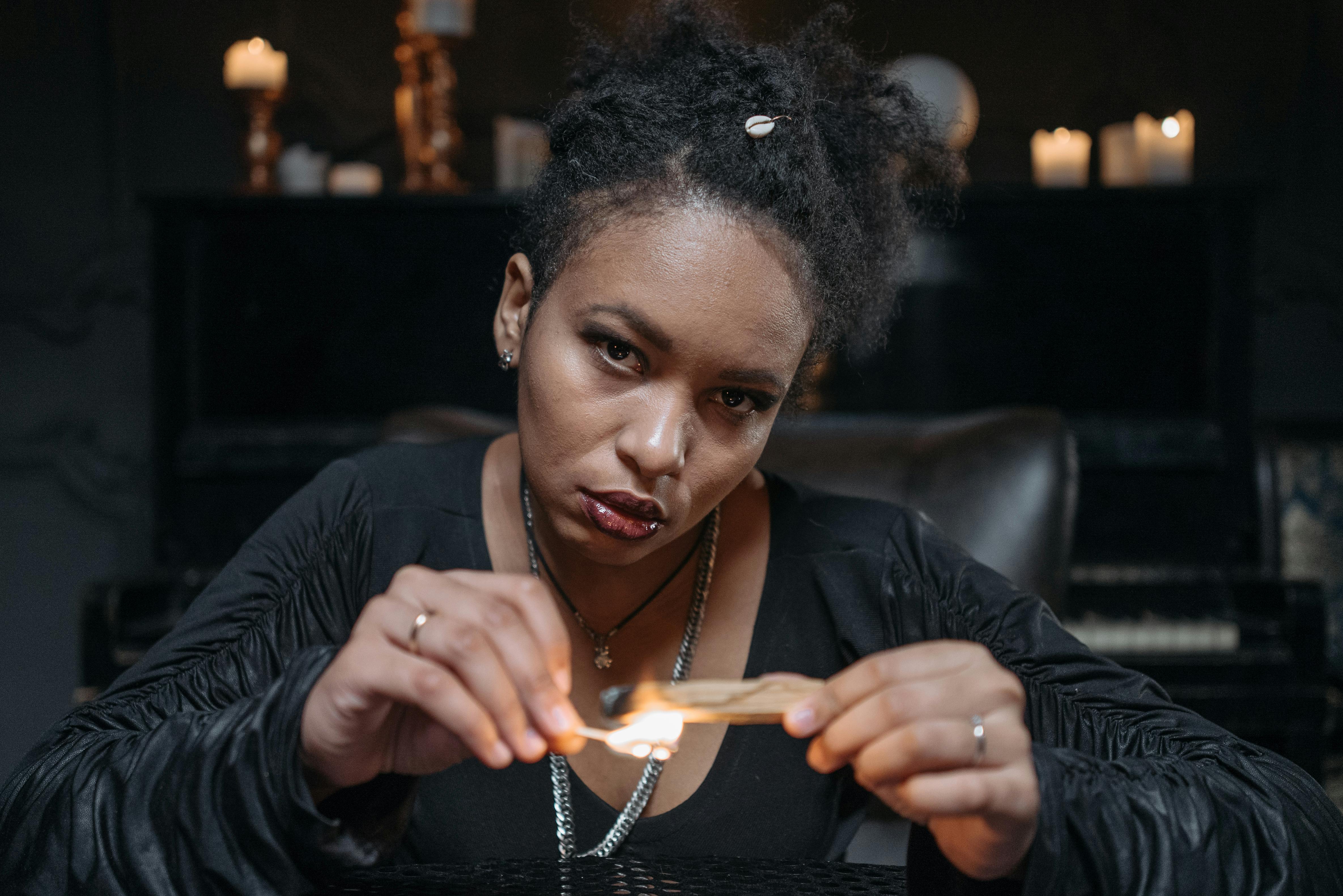 Close-up of a woman lighting a matchstick in a moody indoor setting with candles.