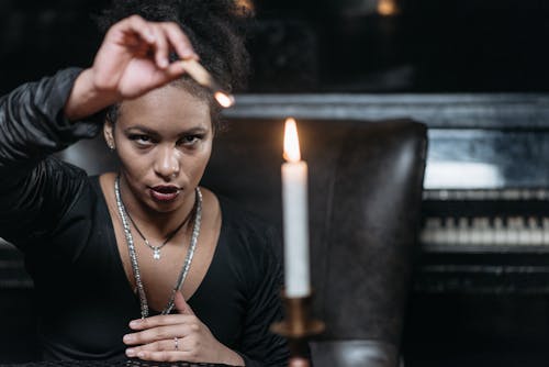 Woman in Black Long Sleeve Shirt Holding Burning Match Stick In Front of a Lighted Candle