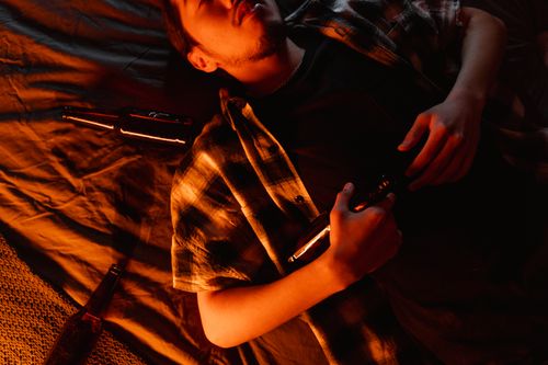 Free A young adult male lies on a blanket in orange light, holding bottles. Stock Photo