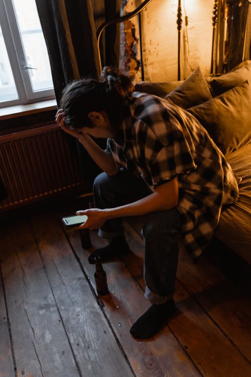 Free A young adult sits indoors, looking contemplative and holding a phone, creating a thoughtful mood. Stock Photo