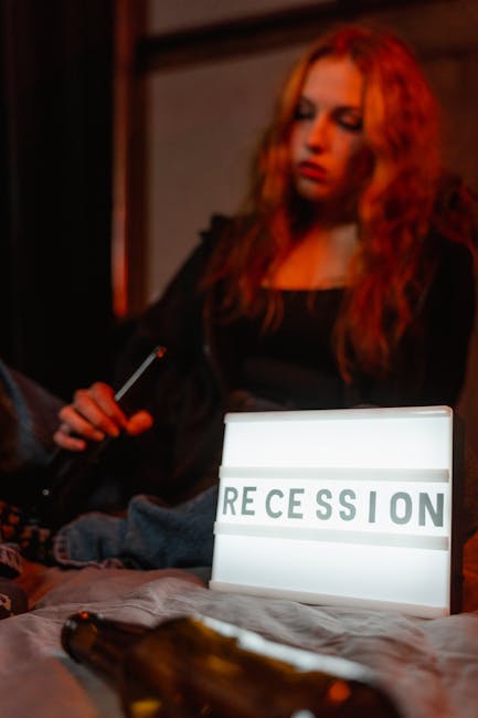 Young woman sitting with sign 'RECESSION' and bottles, reflecting economic downturn.