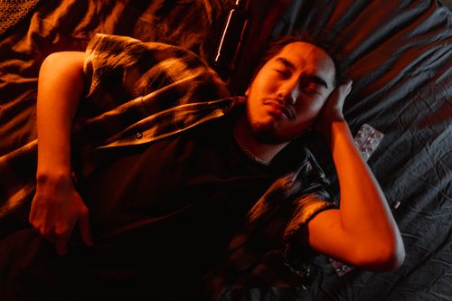 Free A man lies on a bed in orange ambient lighting, creating a relaxed atmosphere. Stock Photo