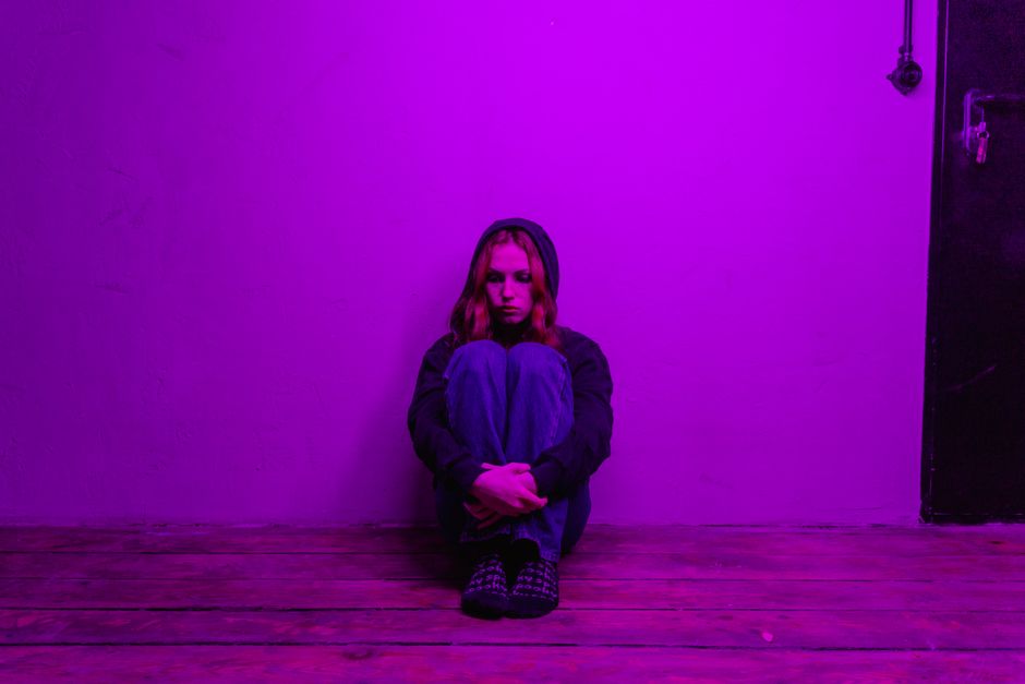 Como Transformar a Ansiedade em Motivação Positiva no Dia a Dia 2 A woman in a hoodie sits alone on the floor, illuminated by purple light indoors.