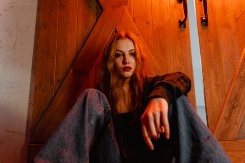 Free Young woman in casual attire sitting against a wooden door, expressing a contemplative mood. Stock Photo