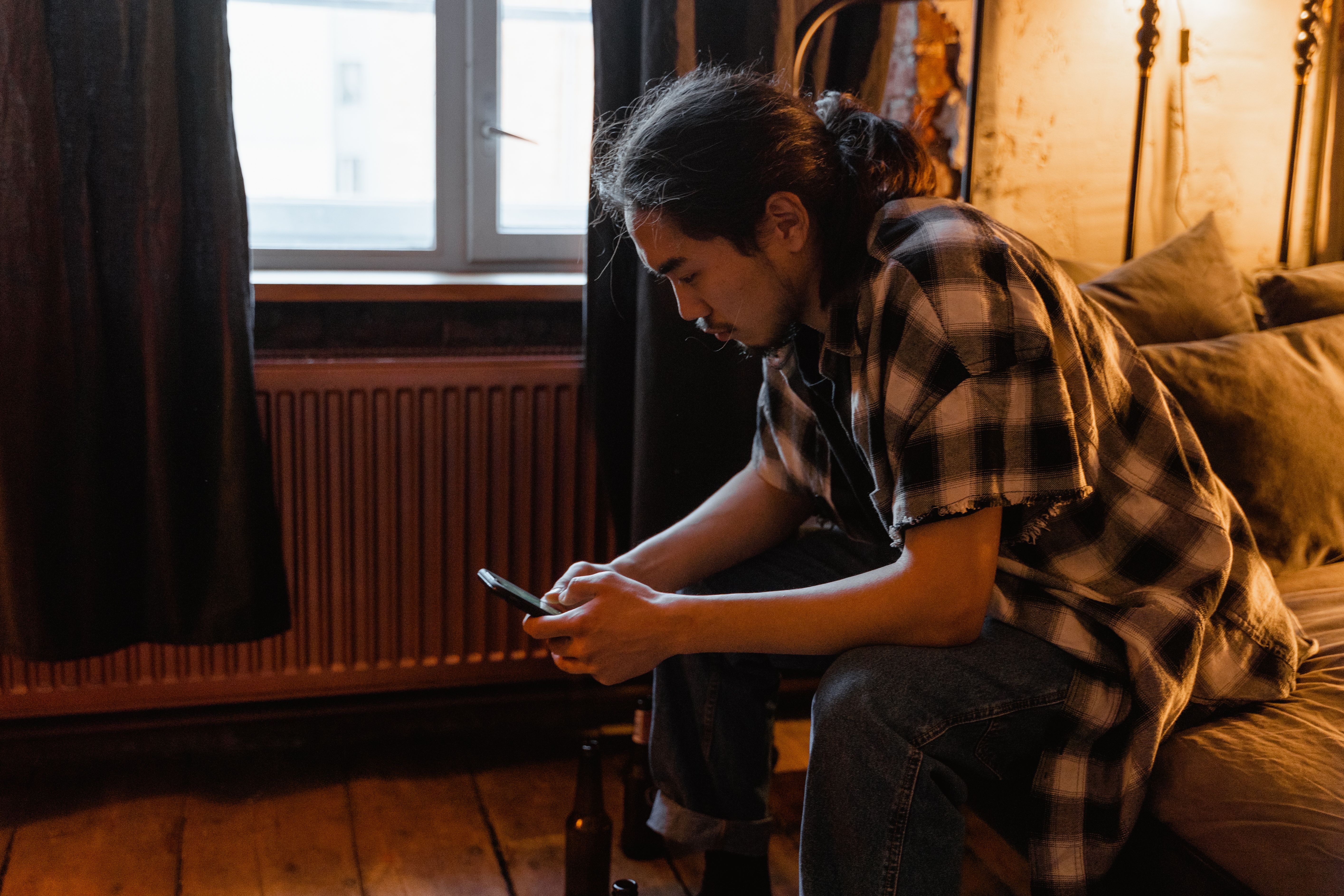 Um homem com uma camisa xadrez usando um smartphone enquanto está sentado em um quarto acolhedor.