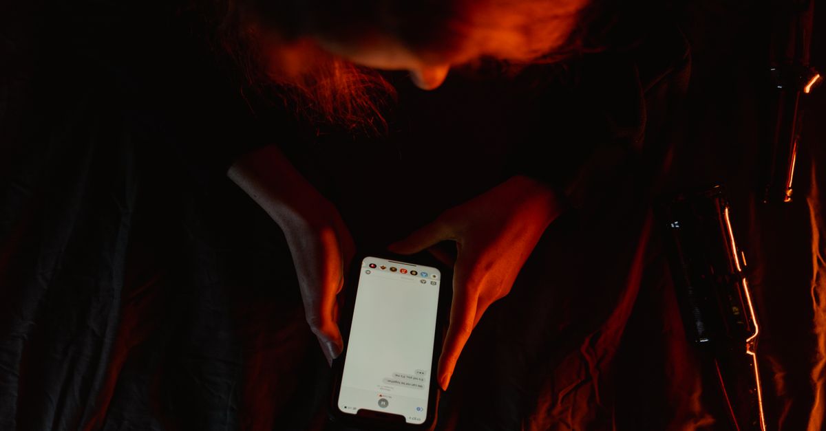 A person using a smartphone in dim, moody lighting with a dark background.