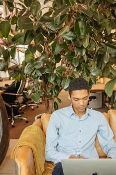 Man working on a laptop in a stylish office with lush indoor plants.